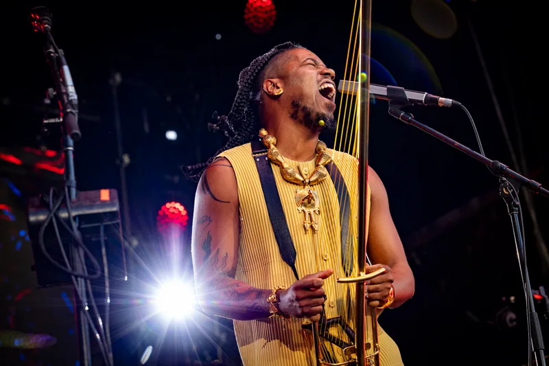 Chief Adjuah singing on stage with a gold-toned stringed instrument