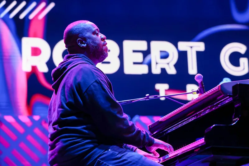 Robert Glasper performing at the piano under blue and magenta lights
